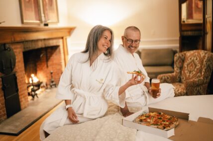 A couple eating pizza on a bed at The Charles Hotel in Niagara-on-the-Lake.